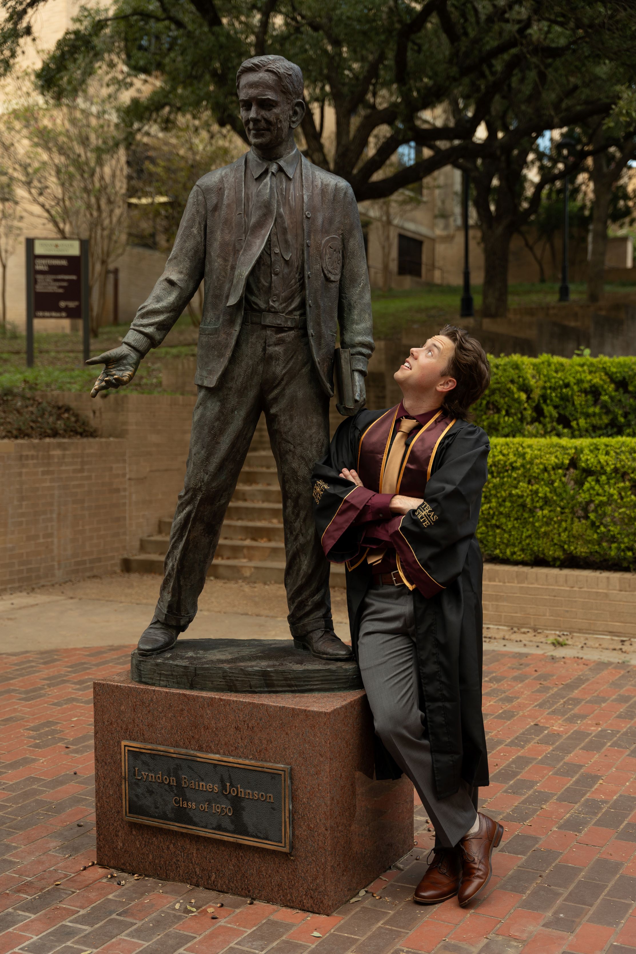 Jack in his graduation gown looking up at a statue of President LBJ